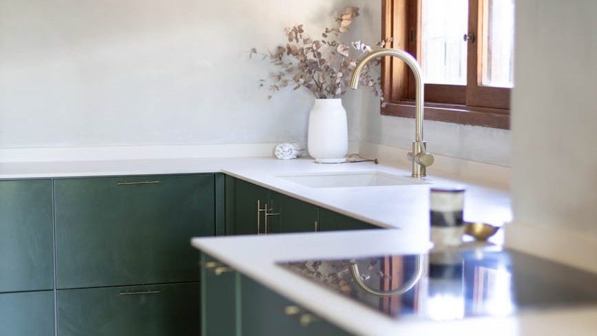 A clean kitchen with natural light through a window and green cupboards